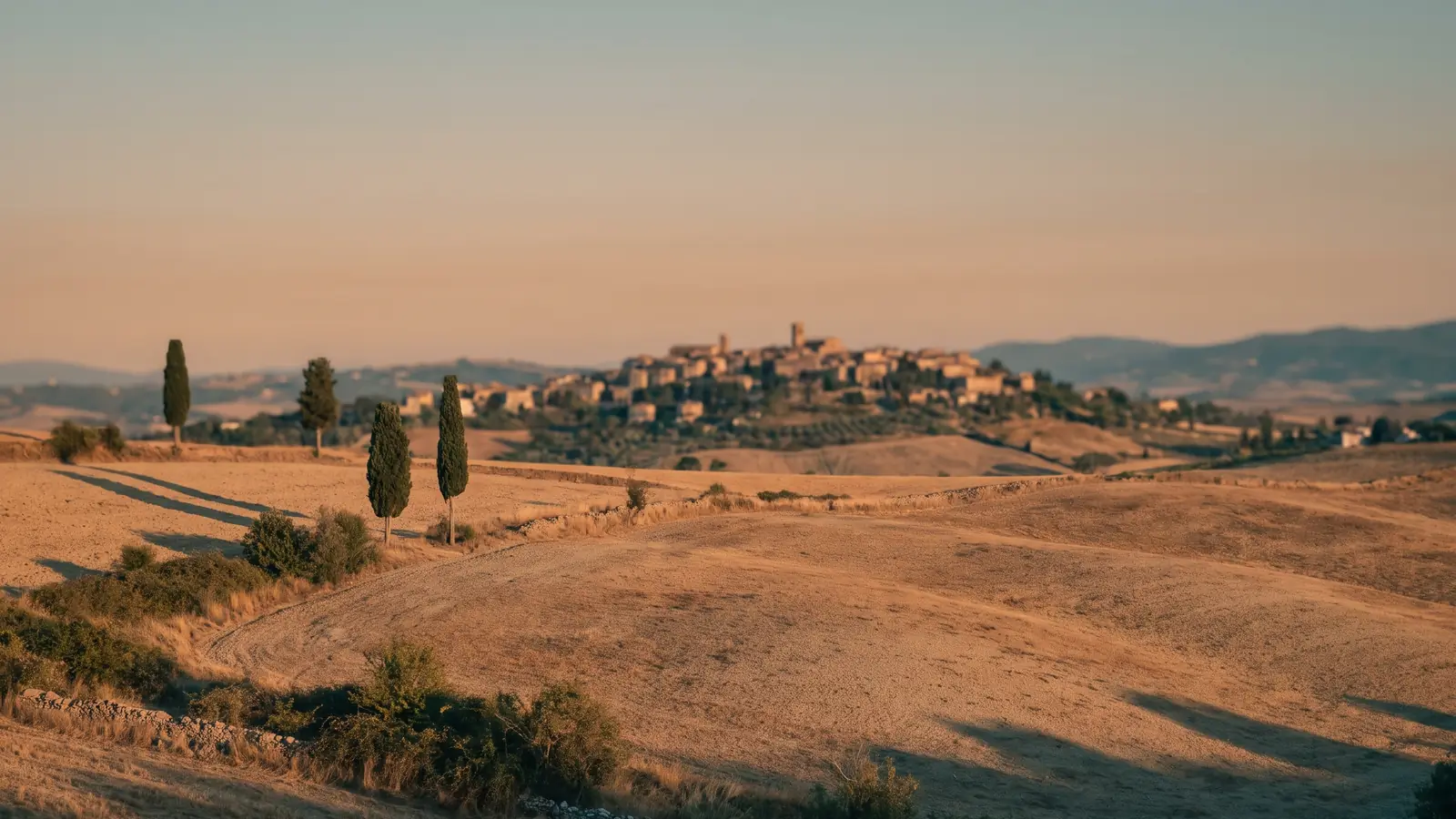 Colline dorate con cipressi e un borgo sullo sfondo, al tramonto